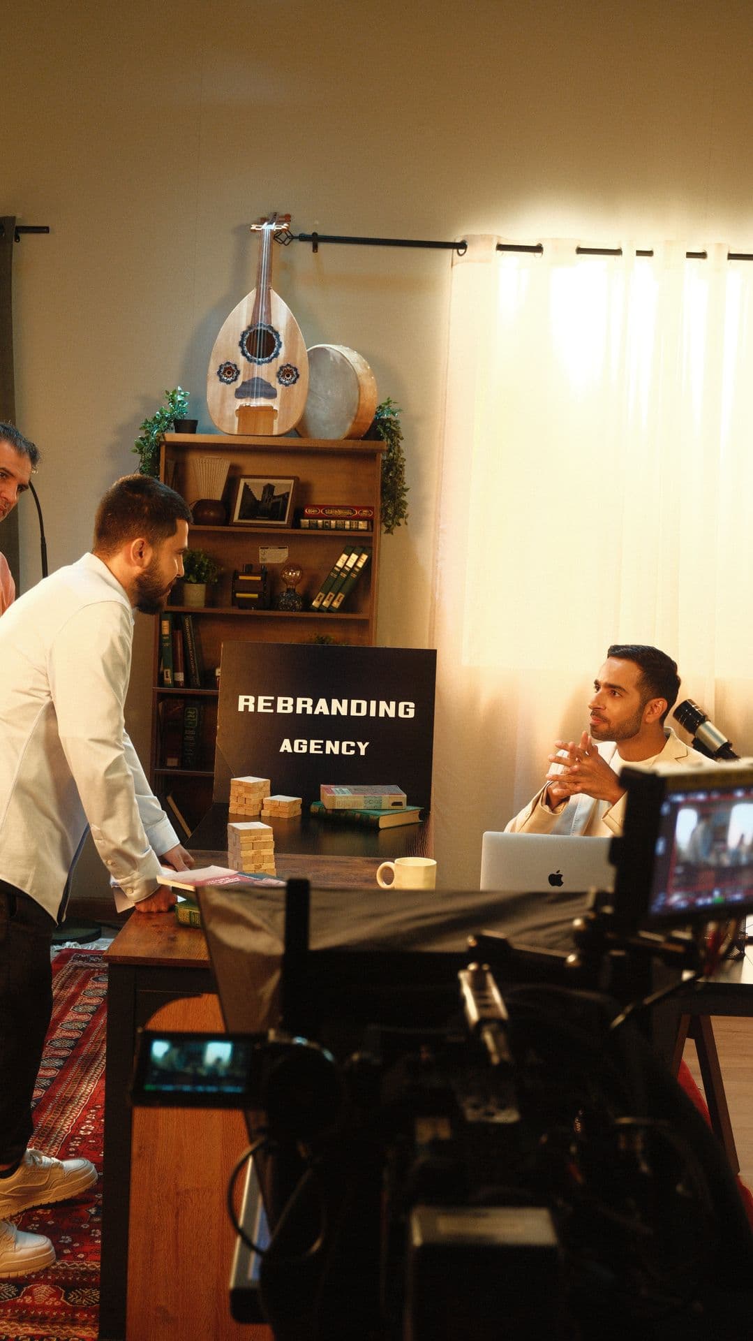 A presenter at a desk seen past a monitor on set
