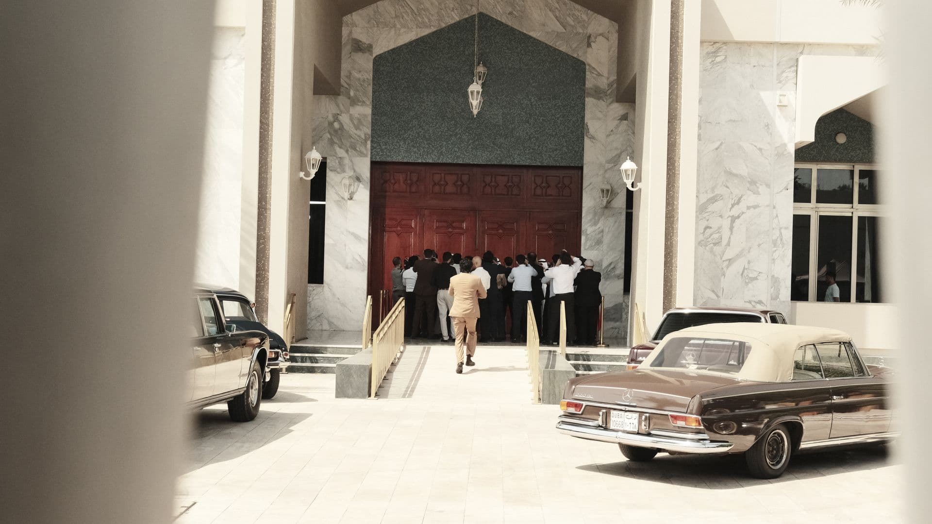 A classic car in front of a red door with a crowd