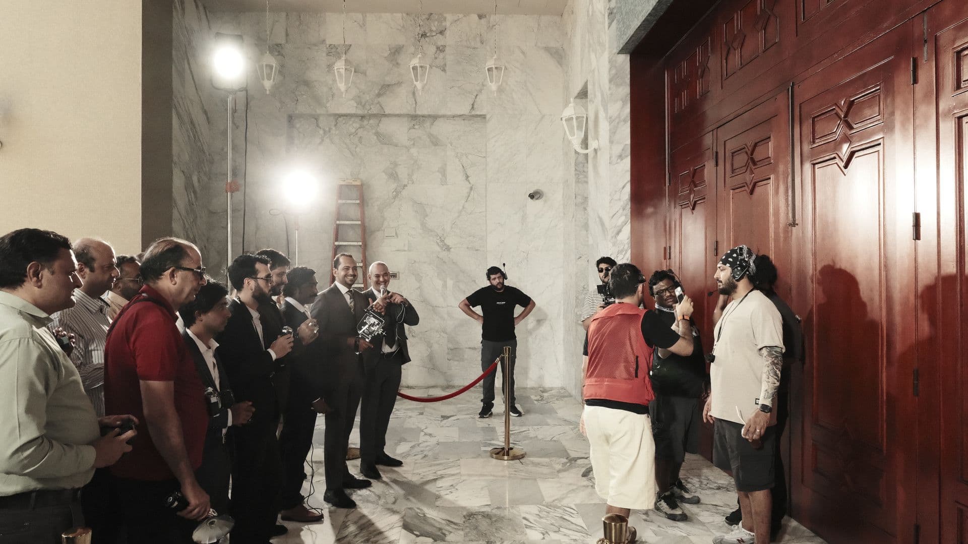 A press crowd in a marble hall by a red door