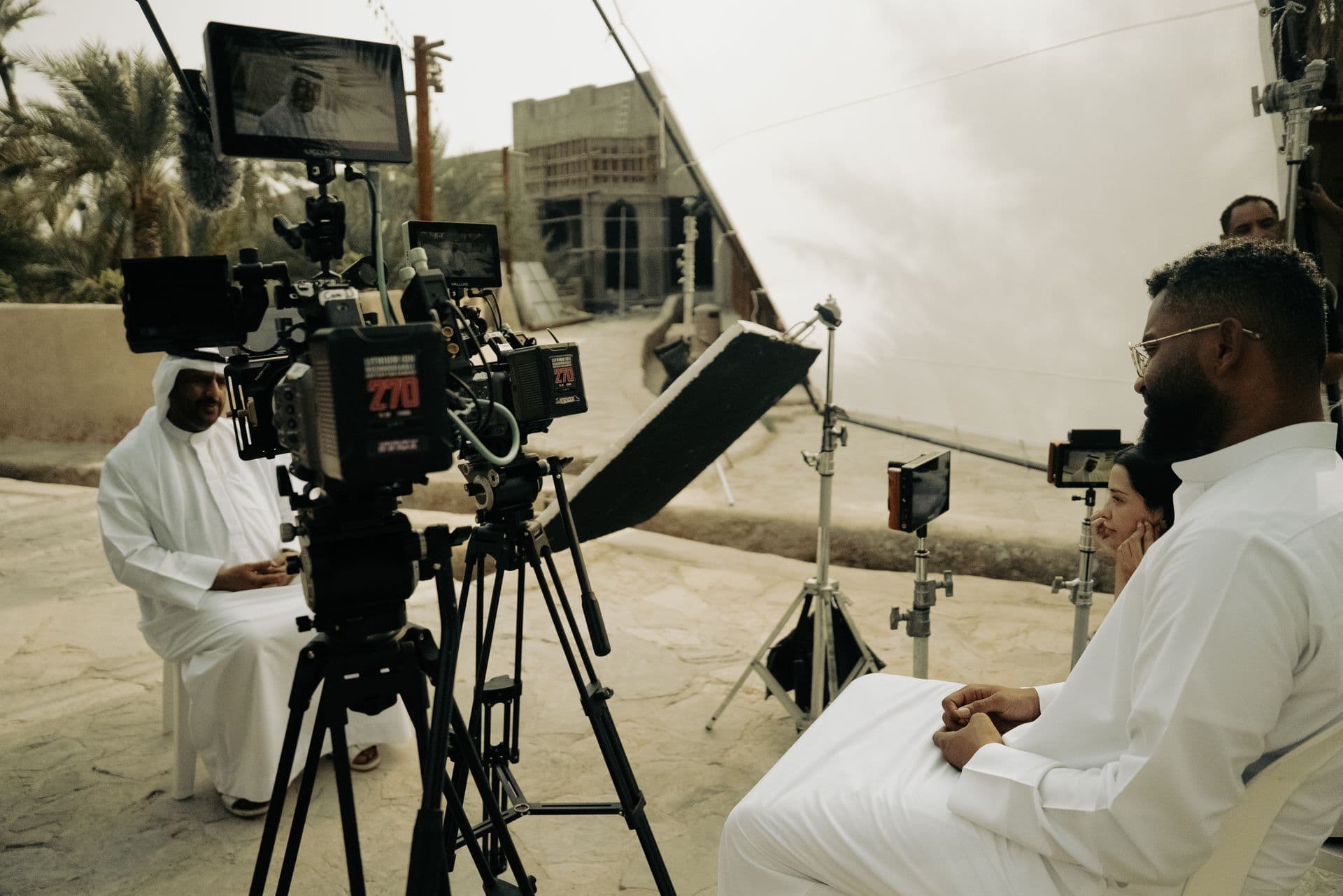 A cinema camera facing an interviewee in a palm oasis
